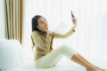 在室内卧室的床上使用手机智能手机的年轻女图片