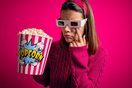 年轻漂亮的女孩用3d眼镜吃爆米花的盒子看电影指着眼睛看着你的手势图片