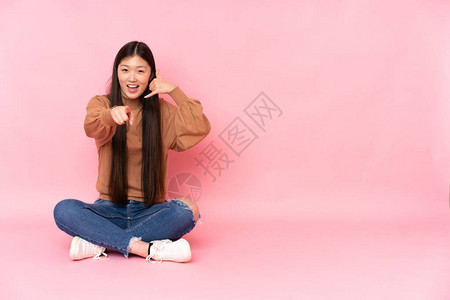 坐在地板上被粉红背景孤立的年轻女图片