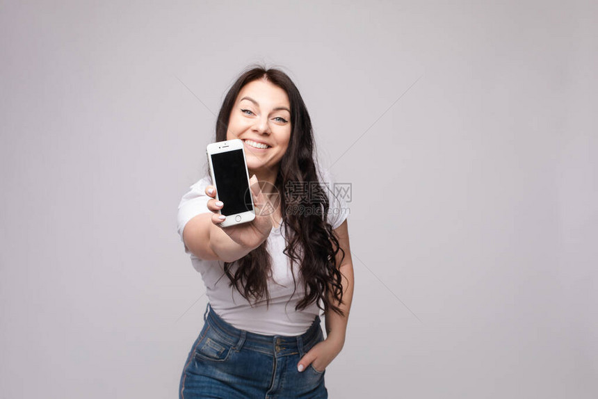 美丽的白种黑发女人的工作室肖像在图案整体用食指着她的智能手机她确定或确定某事图片