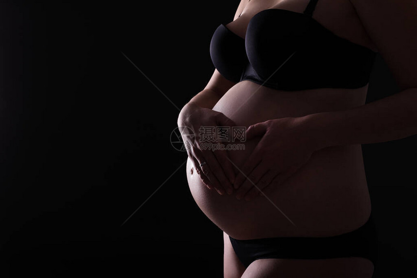 黑色背景下手放在怀孕的肚子上图片
