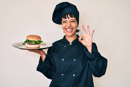 美丽的黑发女厨师拿着汉堡包用手指做好标记笑着亲图片