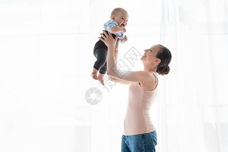 快乐的母亲抱着双臂看着可爱的婴儿子图片