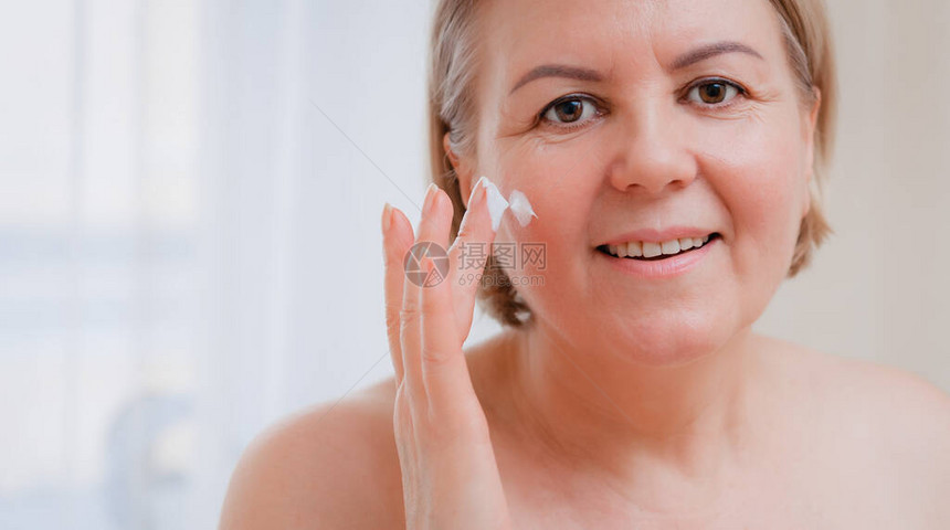 高级女抗衰老乳液对抗黑眼圈快乐的成熟女人使用美容霜来隐藏皱纹一位女士使图片