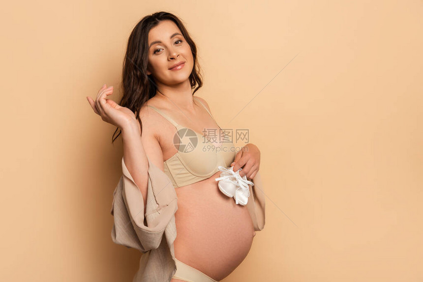 穿着内衣的年轻孕妇带着婴儿靴子同时观图片