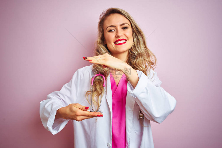 年轻漂亮的女医生在粉红色的孤立背景上使用听诊器图片