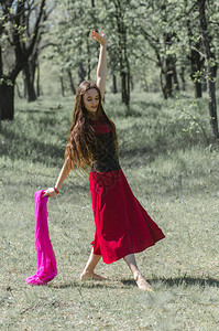 穿红裙子长发的年轻美女在森林里跳背景图片
