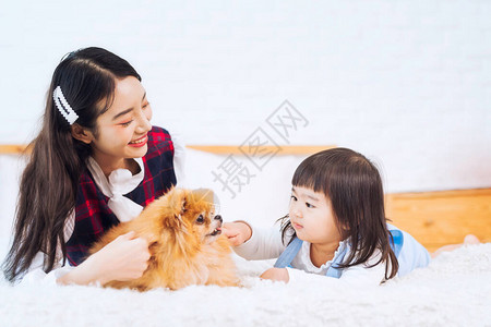 亚洲女孩和年轻女人以及小狗坐在卧室的床上图片