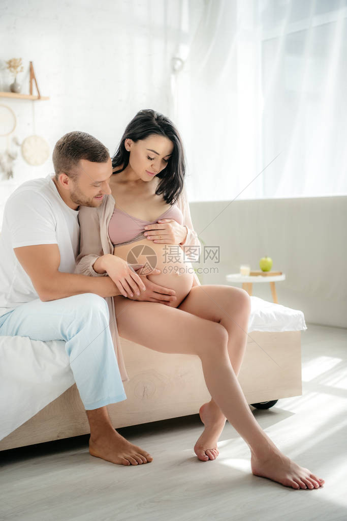 快乐的丈夫在睡床上时拥抱其怀孕妻子图片