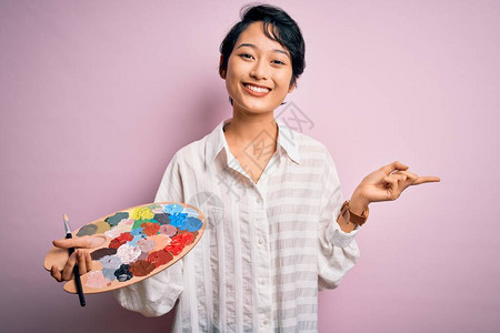 年轻漂亮的艺术家用画笔和调色板作画图片