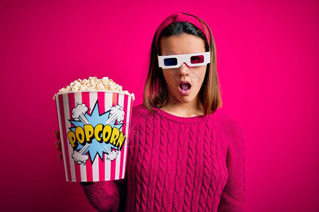 年轻美女在看电影时带着3D杯子吃着盒子的爆米花面对惊吓图片