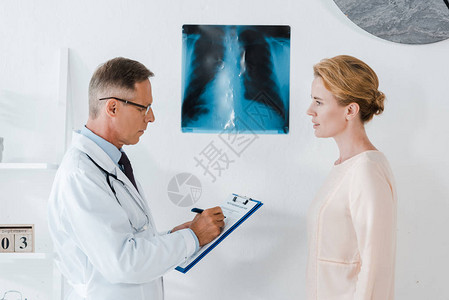 在接近X光的剪贴板上和在诊所工作的妇图片