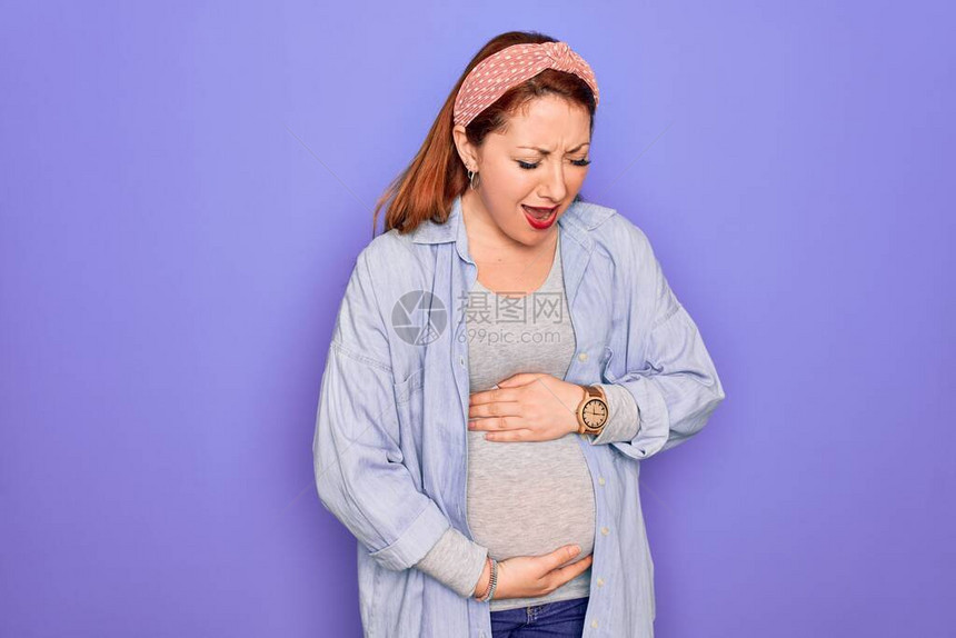 年轻美丽的红发孕妇在孤立的紫色背景中等待婴儿图片