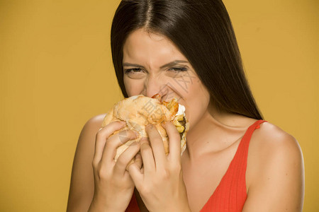 在黄色背景上吃汉堡的年轻贪婪女人图片