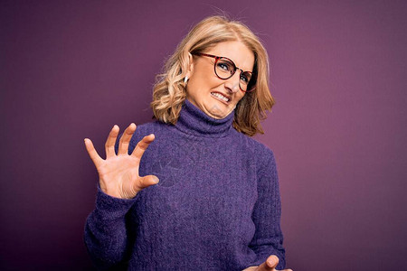 中年金发美女穿着休闲紫色高领毛衣和眼镜厌恶的表情图片