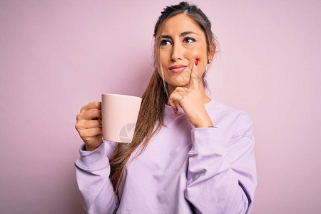 年轻漂亮的褐发女人在孤立的粉红色背景上喝杯咖啡图片
