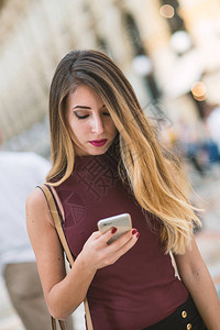 在意大利米兰使用智能手机户外的金发年轻女子肖像图片