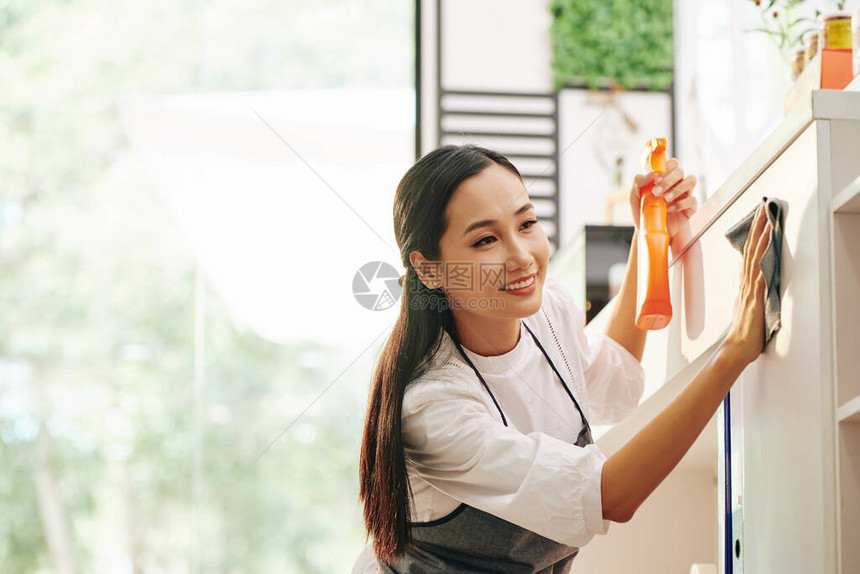 相当积极的亚洲年轻女在柜台上喷洒洗涤剂早上给咖啡厅消毒时用图片