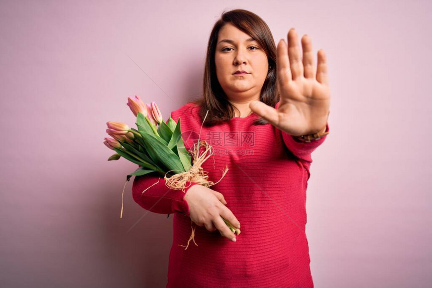 美丽的加上大小的女人拿着浪漫的天然郁金香花束在粉红色的背景上停止用手掌脸上带着消极和严肃的图片