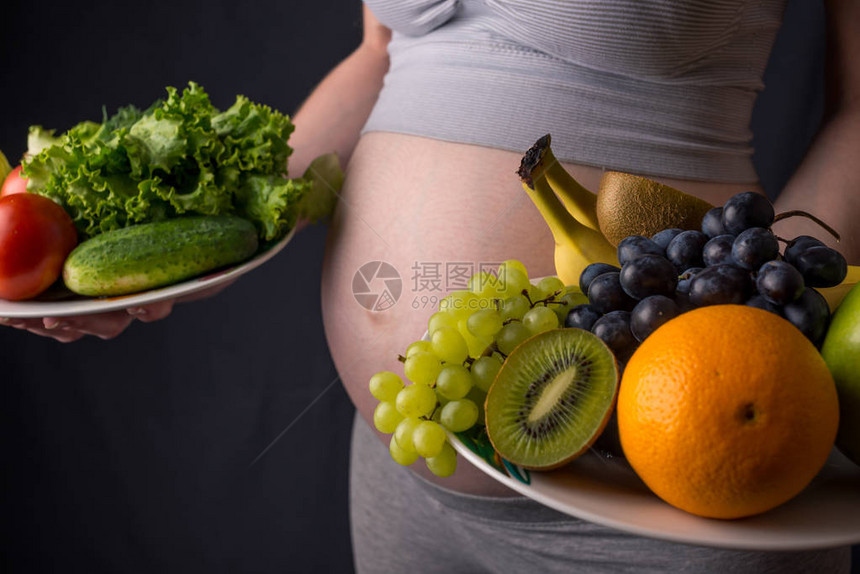 一个有肚子的孕妇手里拿着一盘水果和蔬菜孕期体重控制和健图片