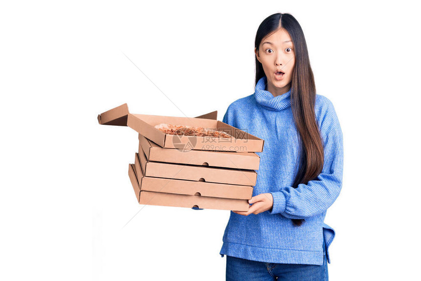 年轻美丽的女人拿着意大利披萨的纸板盒惊吓并用张开的嘴吃惊地讶于惊喜图片