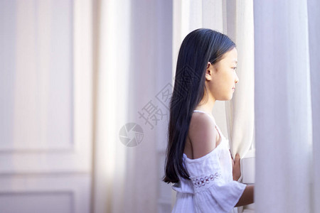 9岁的亚洲小女孩站在窗前向外看图片