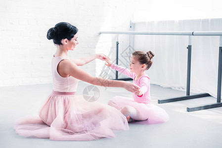 芭蕾舞老师和穿着粉色短裙的小学生在芭蕾舞学校训练时坐着手图片