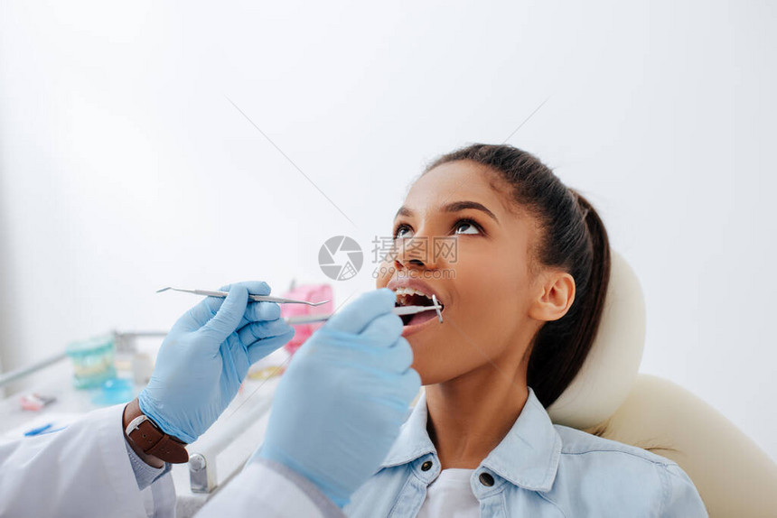 戴着乳胶手套的牙医拿着牙科设备靠近张开嘴和牙套的非图片