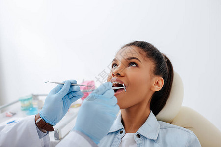 戴着乳胶手套的牙医拿着牙科设备靠近张开嘴和牙套的非图片