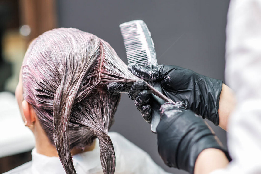 美发师的近景是用黑色手套给顾客的头发涂上颜色图片
