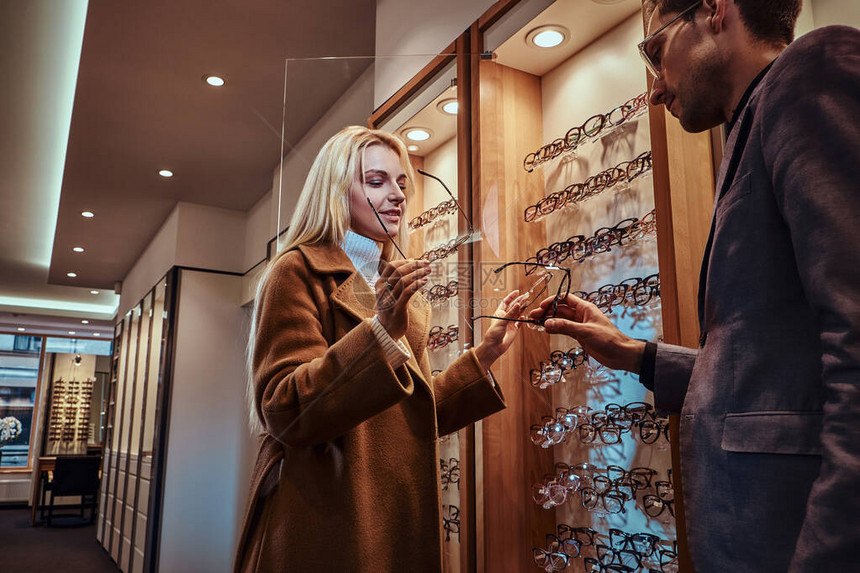男专业顾问正在帮助在光学商店为女客户选择新的眼镜图片
