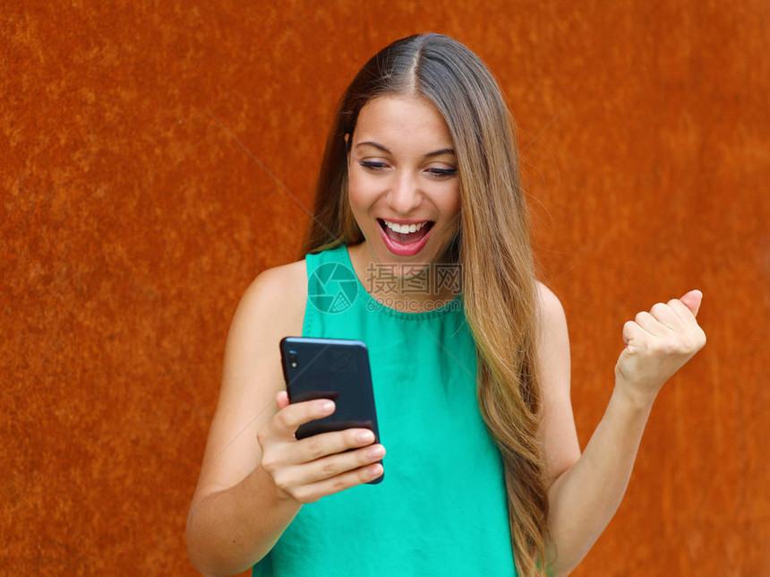 获胜的年轻女子看着她的智能手机庆祝胜利用生锈背景举拳图片