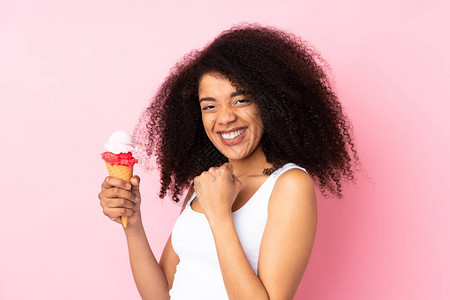 年轻非洲裔美国妇女拿着玉米角冰淇淋孤立在粉红背景上庆图片