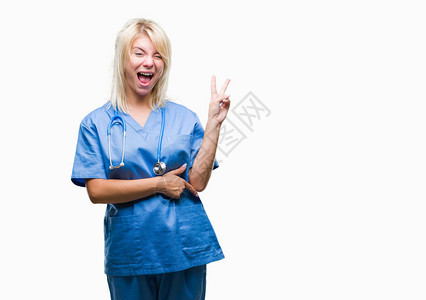 身穿医疗制服的金发年轻女医生在孤立的背景中微笑得脸朝镜头眨眼图片