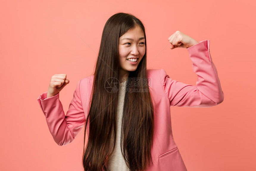 年轻的女商人穿着粉红色西装在胜利后举图片