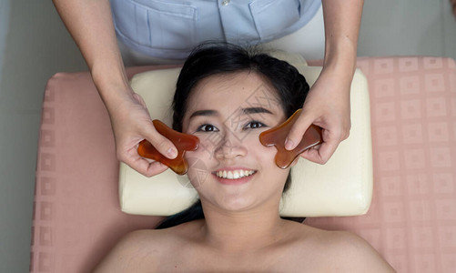 亚洲年轻女在亚洲接受面部刮痧治疗背景图片