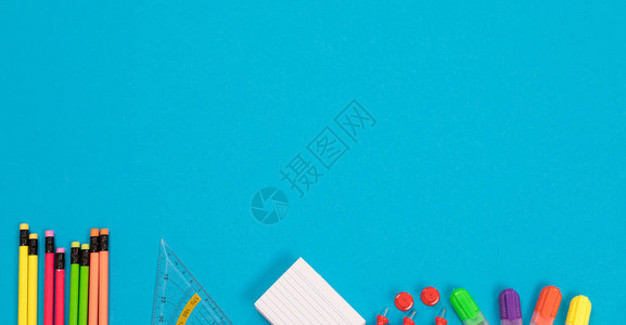 半可见的杂色铅笔三角尺一叠白色草稿纸一组红色别针四个彩色荧光笔的全景图正躺在浅蓝色背景图片