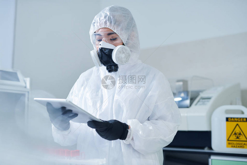 身穿防护服和呼吸面罩的忙碌实验室生物学家在检查测试结果时使用图片