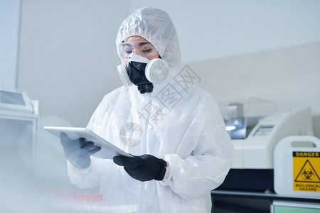 身穿防护服和呼吸面罩的忙碌实验室生物学家在检查测试结果时使用图片