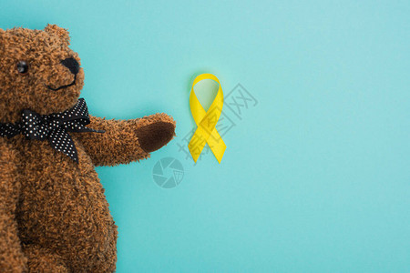 蓝色背景上带弓和黄丝带的泰迪熊的顶视图图片