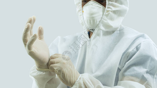 戴面罩和白生物防护西装的医生将乳胶手套放在白图片