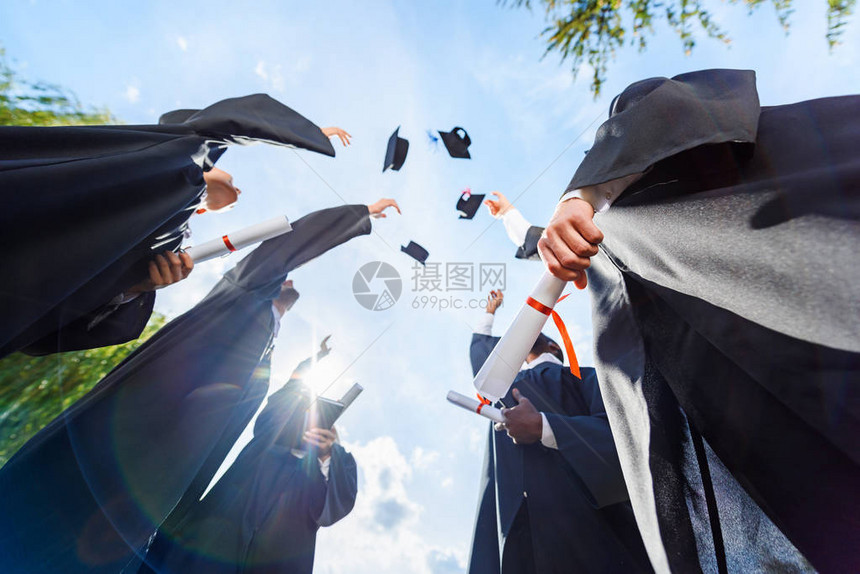 毕业学生在蓝天前扔帽子的底视图图片