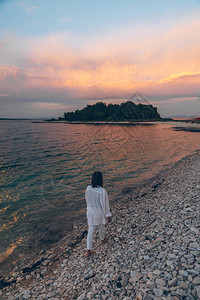 在海滩上散步的年轻美女看着海面上的日落复制太空图片