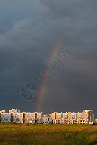 高楼大厦在太阳的金黄光芒反对风雨如磐的天空和彩虹的复合体城市图片