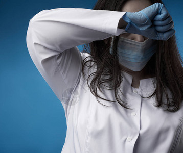 身着白大衣蓝乳胶手套和面罩的年轻女医生站在蓝色背景上图片