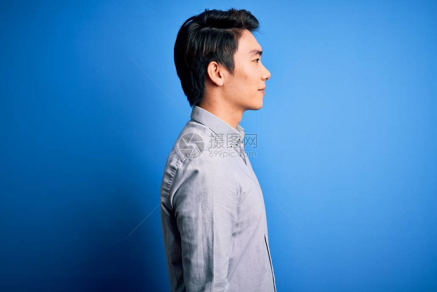 身穿轻便衬衫的英俊男士站在孤立的蓝底背景上站着一旁放松姿势和自然面貌充图片