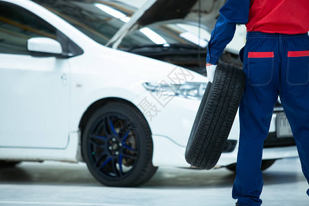 身穿制服的亚洲机械工在汽车修理中心工作时持车轮胎站着图片