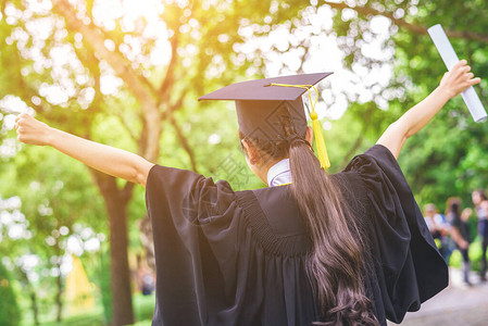 身戴毕业帽子和礼服的毕业生女学生举起手来图片