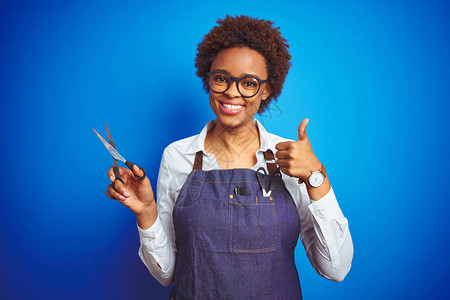 非洲裔美国理发师女人拿着剪刀在蓝色孤立的背景下开心地笑着做好手势图片