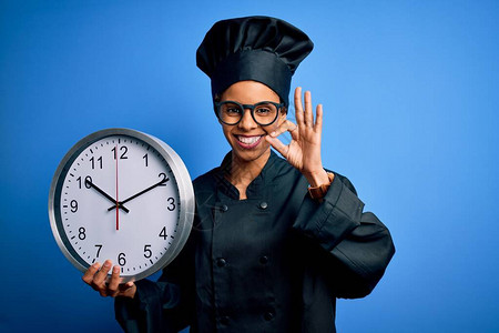 非洲美面包师女身穿烹饪制服戴帽子倒数计时用钟表用手指签好牌子图片